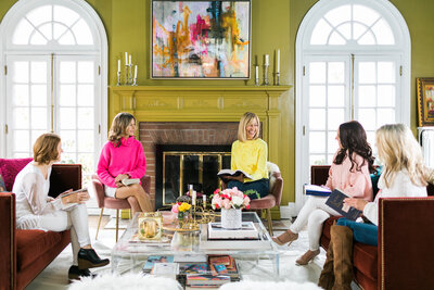 women in coaching session, in a bright vibrant home and wearing bright pink and yellow sweaters seated in a living room with a fireplace in the background