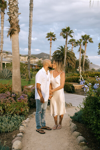 a couple walking among palm trees during their beach engagement  photoshoot in California
