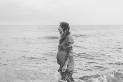 Maternity foto in Leiden aan de zee met een zwangere vrouw die half in het water staat. 