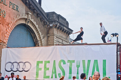 Hannah de Keijzer in a long black dress dancing on scaffolding above an arts and food event.