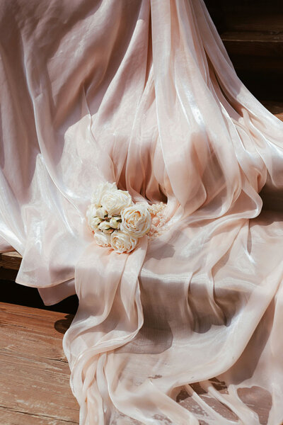 Soft pink wedding dress draped over steps with white roses