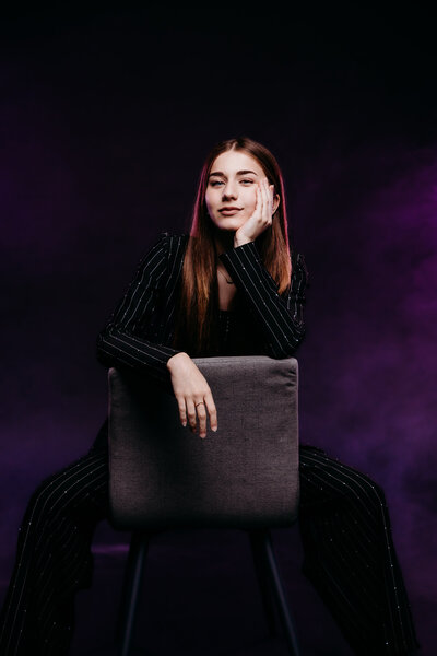 Ionia teen girl sitting backward in a chair with purple background