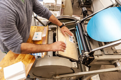 Overhead branding image for Merlina Design featuring a man putting business cards through a press printing machine.