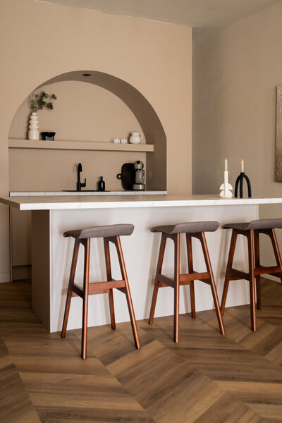 Minimalistisch ingerichte slaapkamer in Studio Laurant met een bed tegen vier bogen aan de hoofdbordzijde en een houten voetenbankje aan de voetenzijde, in een serene en stijlvolle setting.