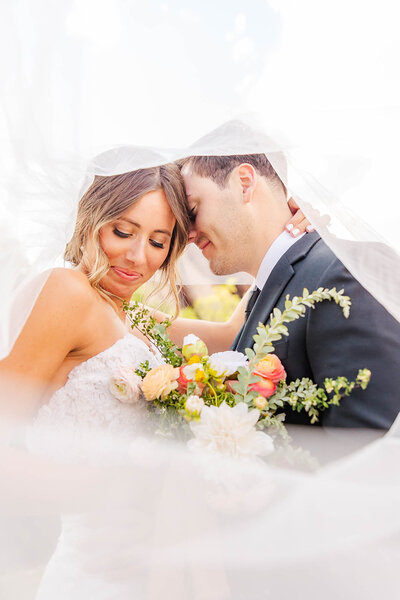 Bride and groom cuddling under brides veil at their romantic wedding in Littleton, Colorado at the Arrowhead Golf Course.