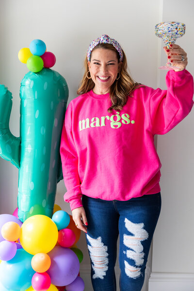 woman with dark hair in pink sweatshirt with margarita