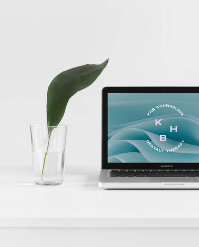 KHB Counseling Gestalt Therapy Alternative Logo on a laptop next to a leaf in a glass  on a desk