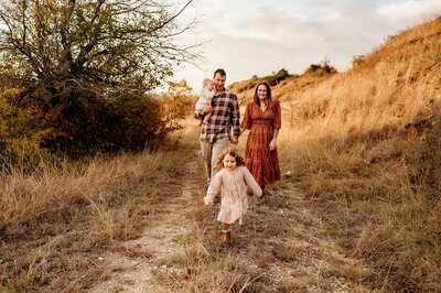 Family having fun with their little ones - big sister is running while mom and dad walk behind enjoying the family session with Paula Goforth Photography in Fort Worth, Texas