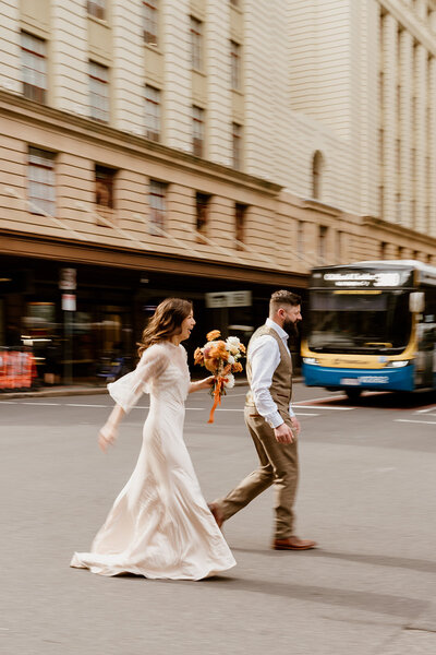 Couple run across an intersection in Brisbane city for their city elopement - Brisbane Elopement photographer
