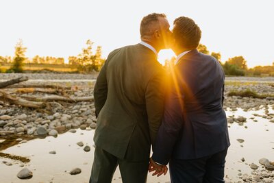 LGBTQ+ Couple holds hands and kiss with a beautiful bright yellow sunset.