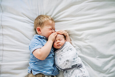 big brother kissing little brother swaddled cozy at home .