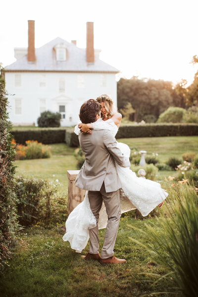 A groom lifting up his bride and spinning her around in a garden.