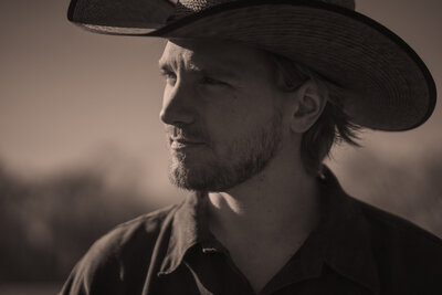 Cowboy stares off into the sun surrounded by rescue horses.