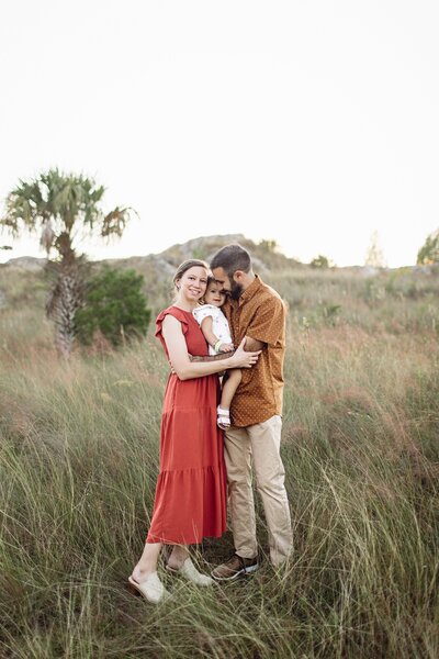 Family photography family photo wife holding child with husband in field In Tampa Bay, Florida Nadine B Photography