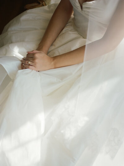 painterly natural wedding photography, a bride's hands rest on her gown, her antique gold ring glinting in morning sun