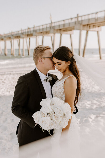 newlyweds pose on beach in front of pier