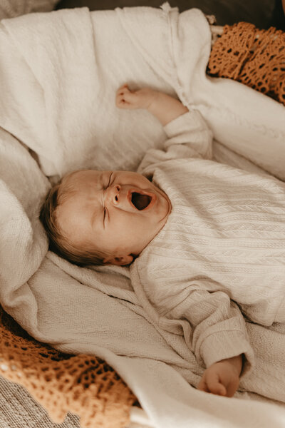 New mother cradling newborn baby while sitting in nursery rocking chair, captured during lifestyle newborn session – Morristown, NJ