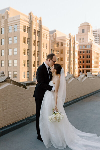 A bride and a groom kissing on a city rooftop.