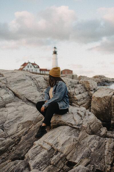 woman sitting on rock with lighthouse in the background