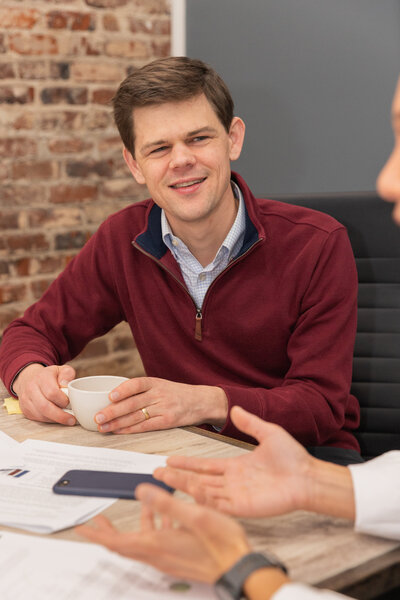 man holding a cup of coffee and listening to someone talking during a business meeting Atlanta brand Photographer