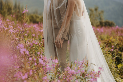 Close-up of a bride’s arms and veil in a purple flower field, capturing romantic wedding day details.