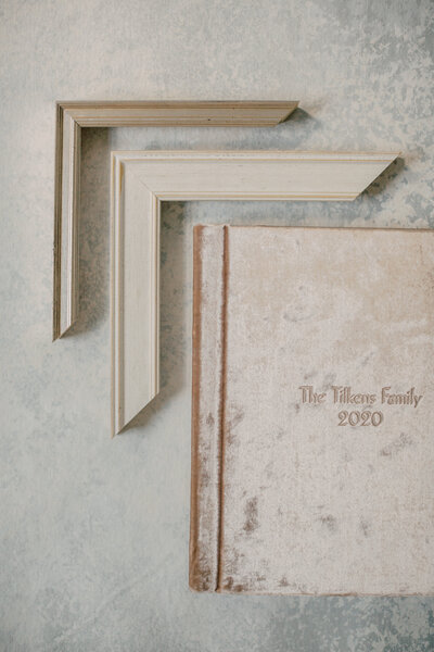 Velvet fine art album lays on blue and gray backdrop with two frame corners