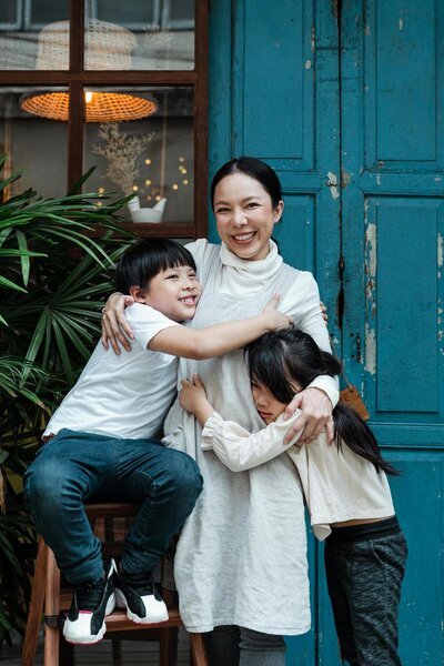 asian family of three hugging and embracing each other in-front of a blue door