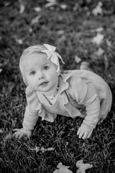 Black and white photo of baby girl crawling on grass with light colored clothes on.