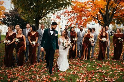 Wedding party strolling through a park blanketed in autumn leaves