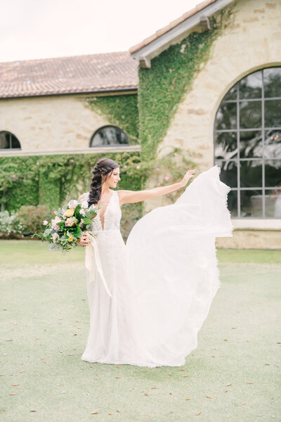 Beautiful bride holds her bouquet and lifts her skirt behind her to blow in the wind
