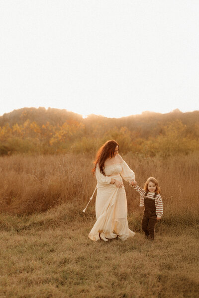 mom and toddler running thought a wheat field at sunset in a golden glow