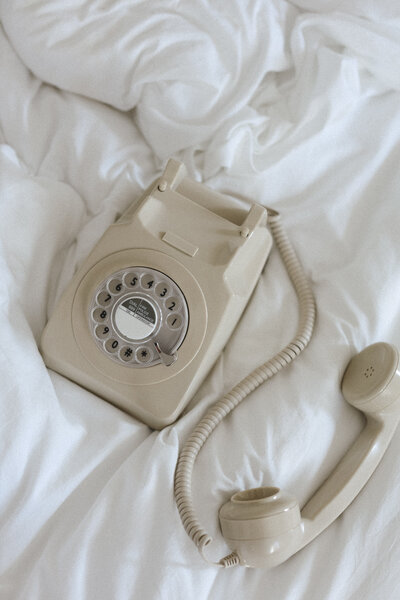 retro hotel phone sitting on bed, receiver off the cradle