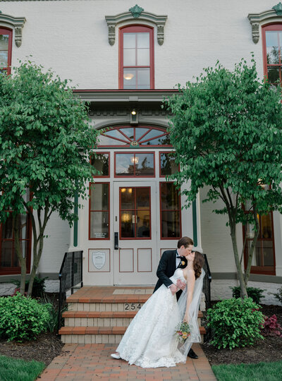 A groom dips and kisses his bride outside by a old building