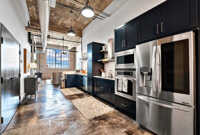 Kitchen with stainless steel appliances and exposed pipe ceiling in this three-bedroom, two-bathroom vacation rental condo in the historic Behrens building in downtown Waco, TX.