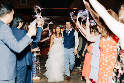 A bride and groom walk through a crowd of guests who are cheering and waving glow sticks, celebrating their wedding indoors. The couple looks joyful and surprised as they head down the aisle, captured by a wedding photographer in Eau Claire.