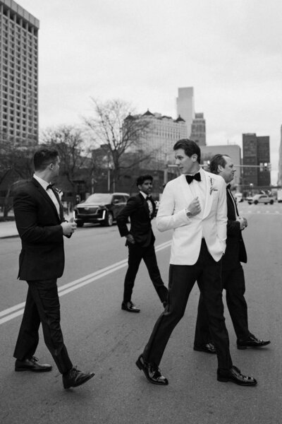 A newlywed and their wedding party dressed in suits walking across the street 