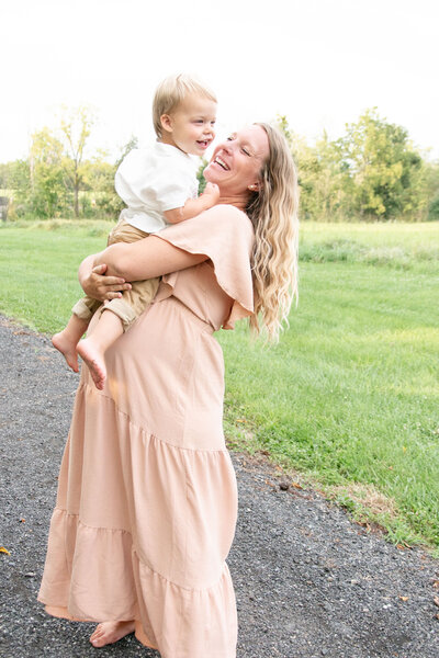 Mom in a pink dress is holding her son in a white shirt.