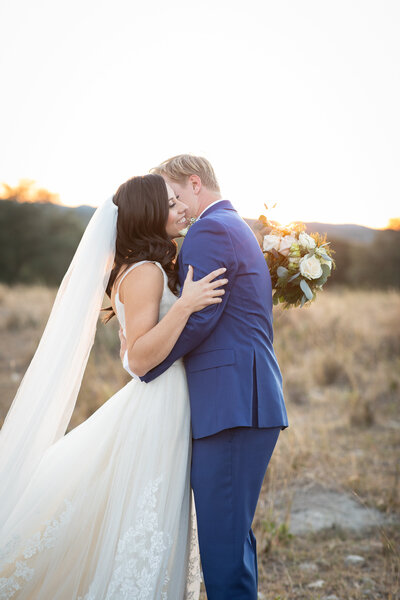 An Austin-based wedding photographer captures a romantic moment as a bride and groom share a tender sunset kiss in a beautiful field.