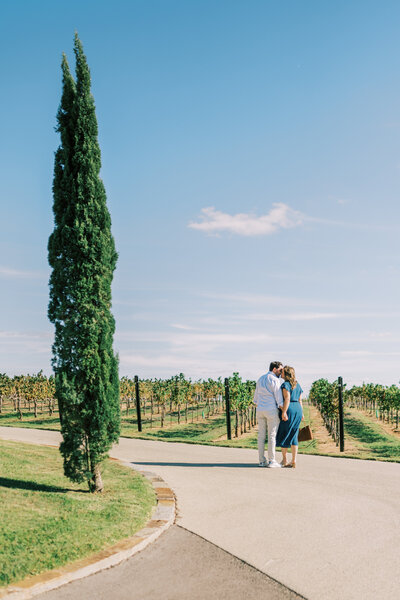 Couple kissing while standing on a path beside a vineyard