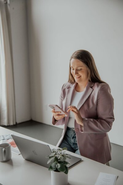 Jessica Young looking at a phone at a desk with laptop