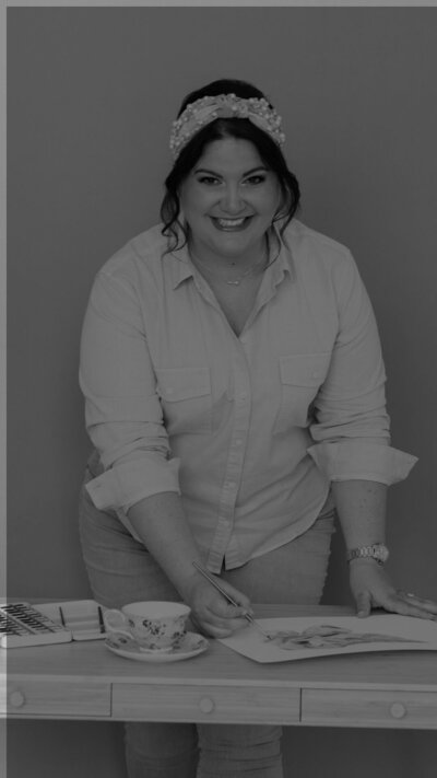 calligrapher smiling at desk with calligraphy tools and tea cup during brand photography session black and white