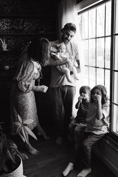 Family of five in front of window father holding infant and two toddlers playing