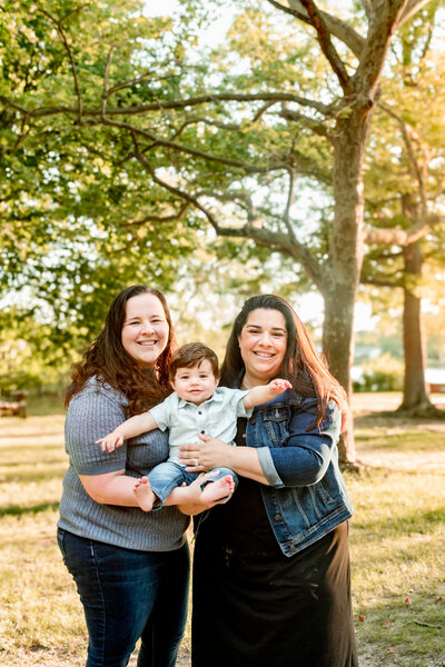 Two moms holding their baby boy at golden hour in a park