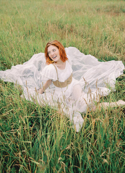 Woman in a flowy white dress sitting in a grassy field