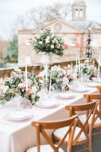 Elegant outdoor table setup with floral centerpieces and candles in front of a historic building