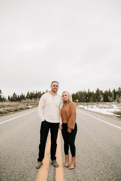 a couple in grand teton national park near the snake river overlook standing next to each other on the road taken by adrian wayment photo