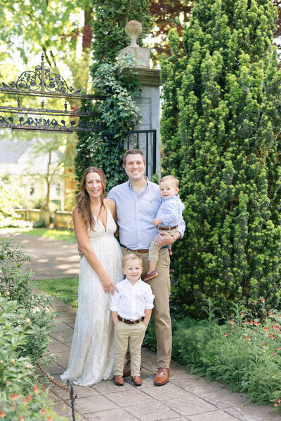 Portrait of a family of four standing in a beautiful garden smiling at the camera taken by newborn photographer missy marshall