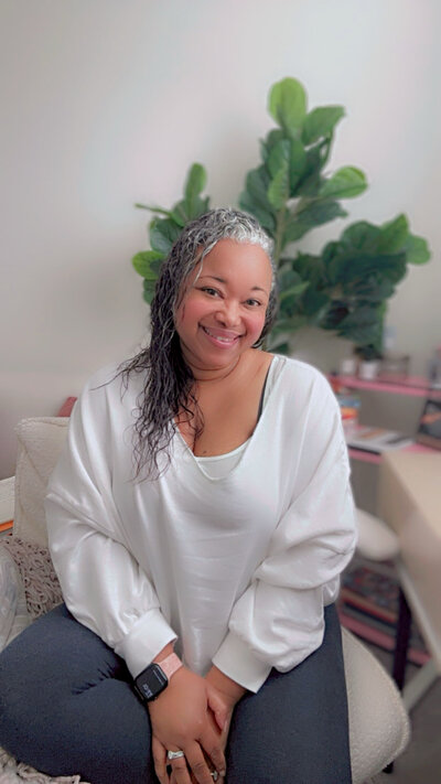 Letitia Hopkins sitting in her office chair wearing a white sweatshirt off one shoulder, smiling confidently and embodying self-love, relaxed alignment, and Main Character Energy as a life, love, and relationship coach guiding women into empowered, fulfilling lives and relationships.