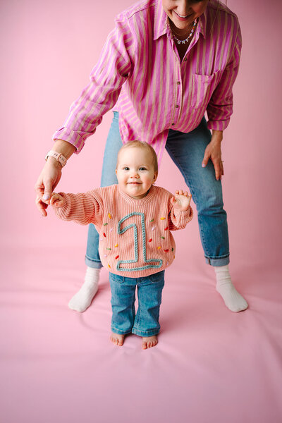 A person holding a small child's hand as they stand and smile 