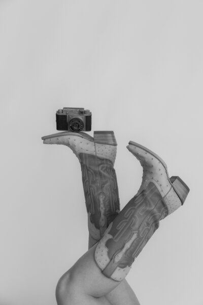 Black and white photo of cowboy boots with a camera resting on top of them